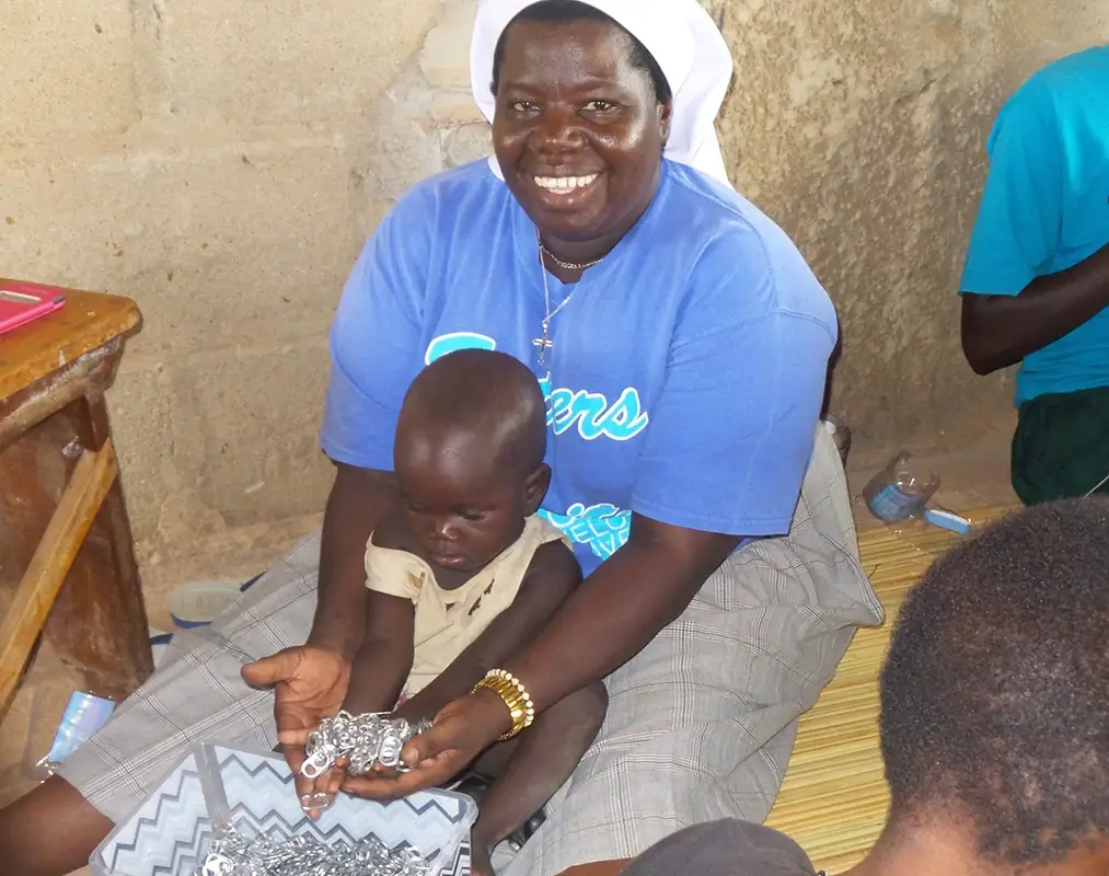 Sister Rosemary holding toddler playing with pop tabs